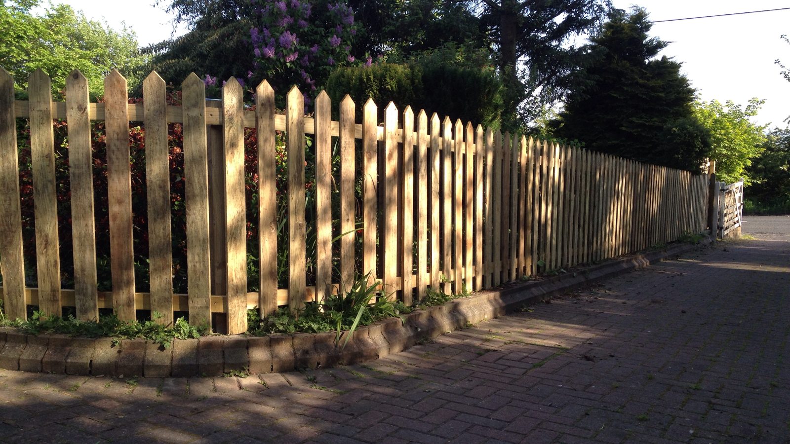 A pointed-top picket fence along a block-paved drive