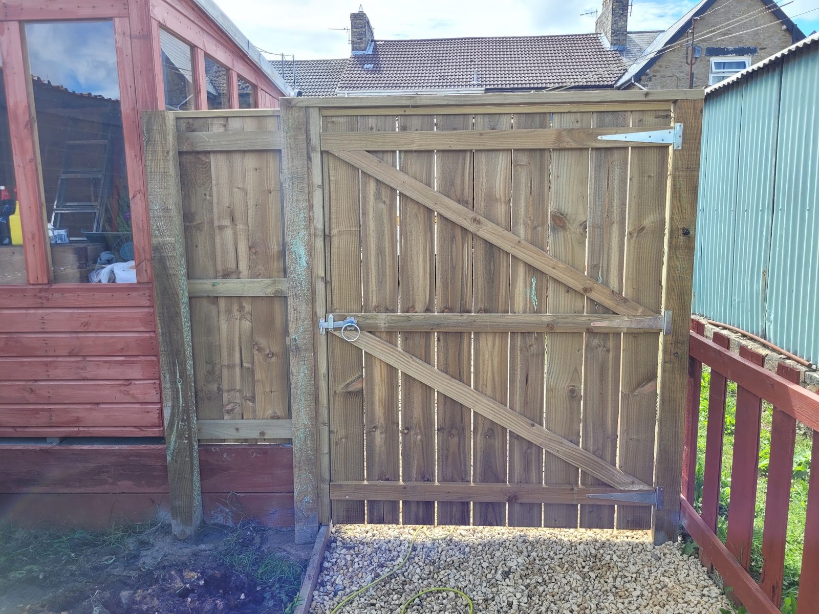 A braced timber gate in its frame beside a summerhouse