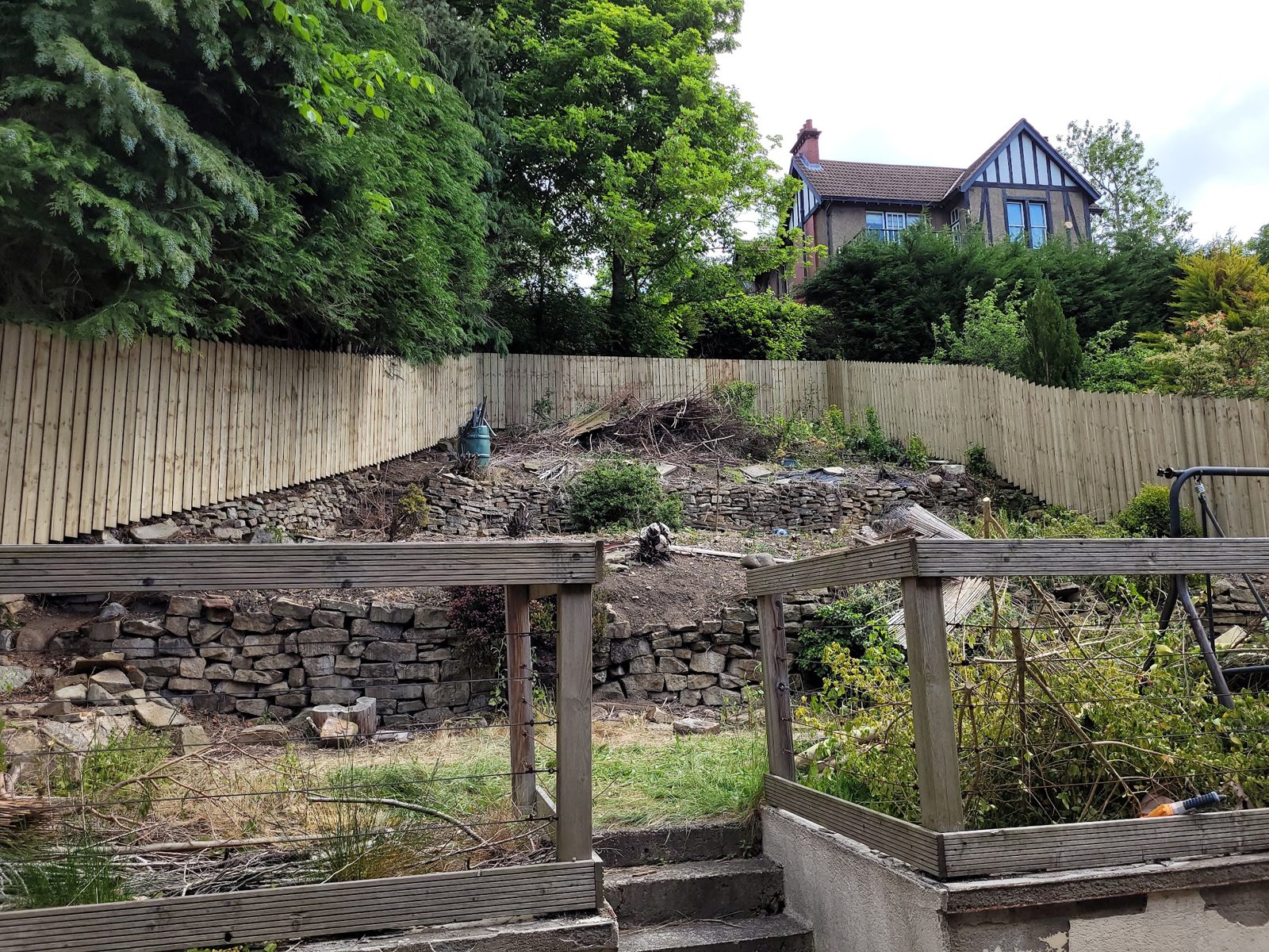 A close-board fence along a sloping garden with stone retaining walls