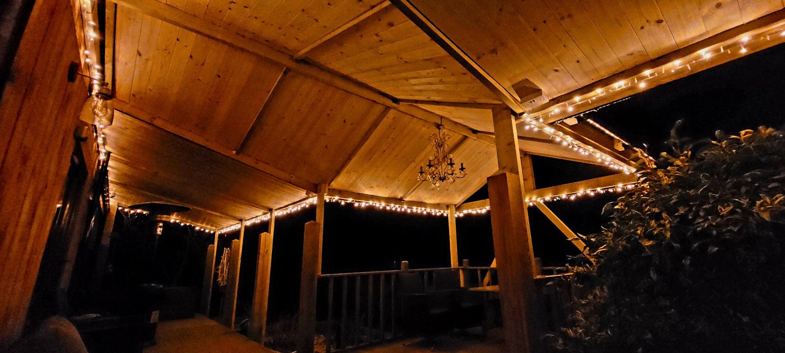 A timber gazebo at night, lit with fairy lights and a chandelier